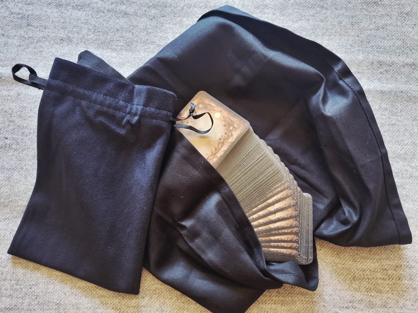 Black velvet drawstring bag next to a matching tarot cloth with the deck fanned across it, on a grey knit throw