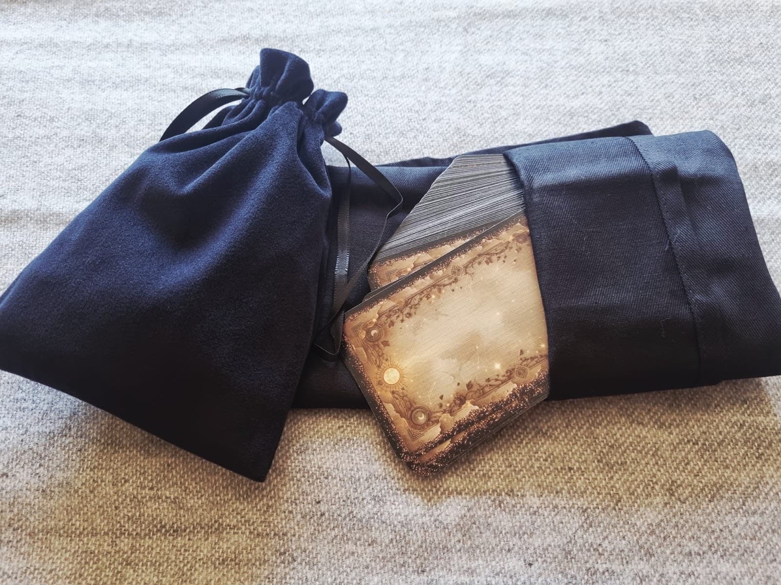 Navy velvet drawstring bag resting on a folded tarot cloth with one gilded tarot card tucked at the front