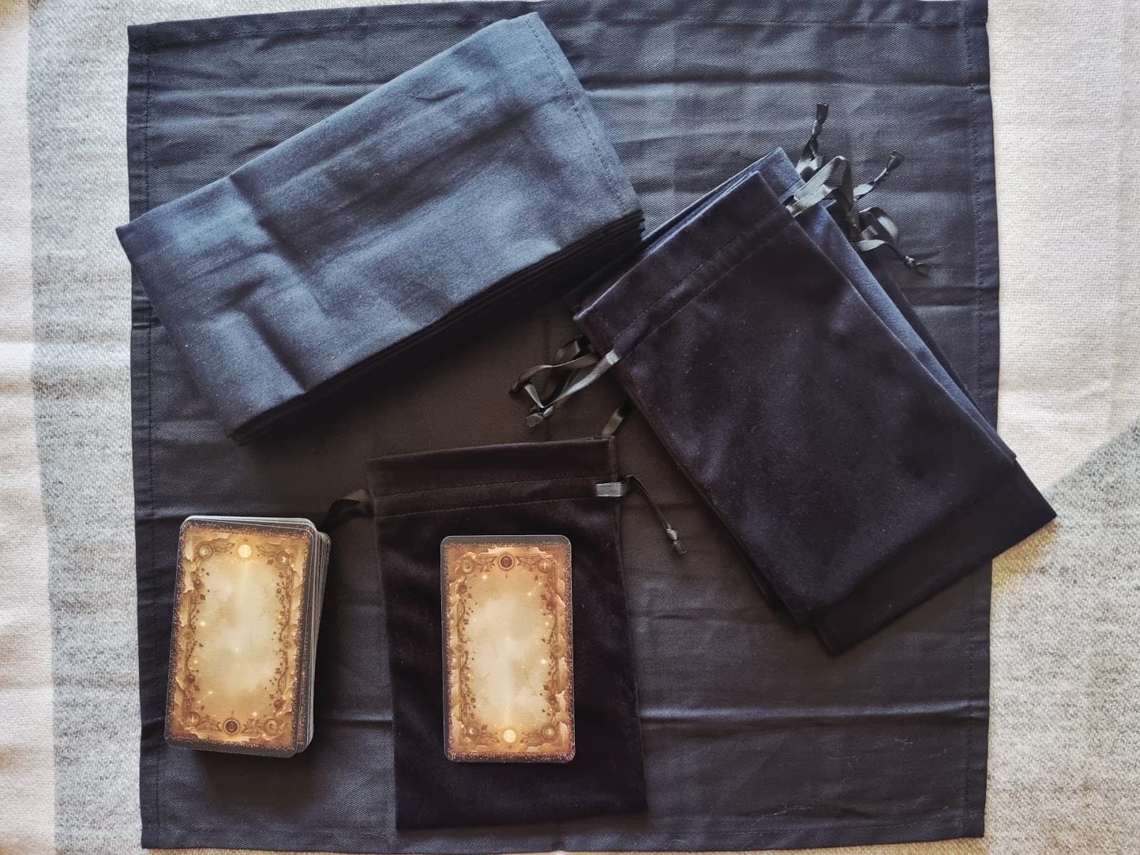 Two tarot bag and cloth colourways in grey-blue and black velvet, shown beside two decks with gilded card backs